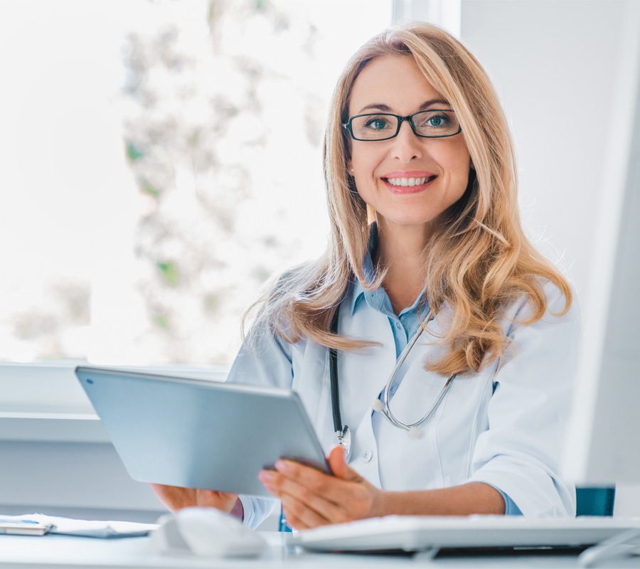 Smiling female doctor sitting at her desk holding digital tablet