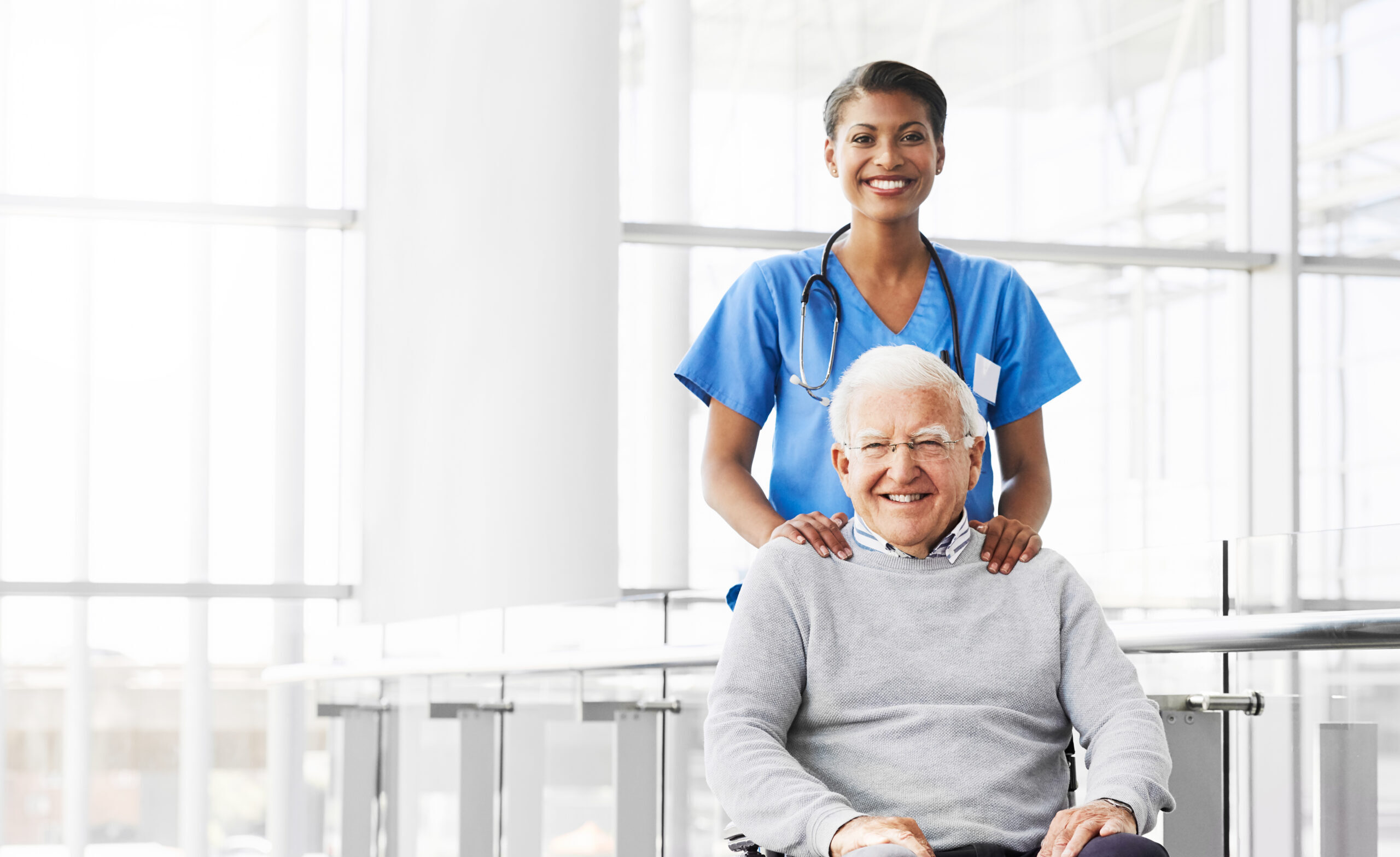 Infermiera con camice azzurro accompagna un signore anziano sulla carrozzina
